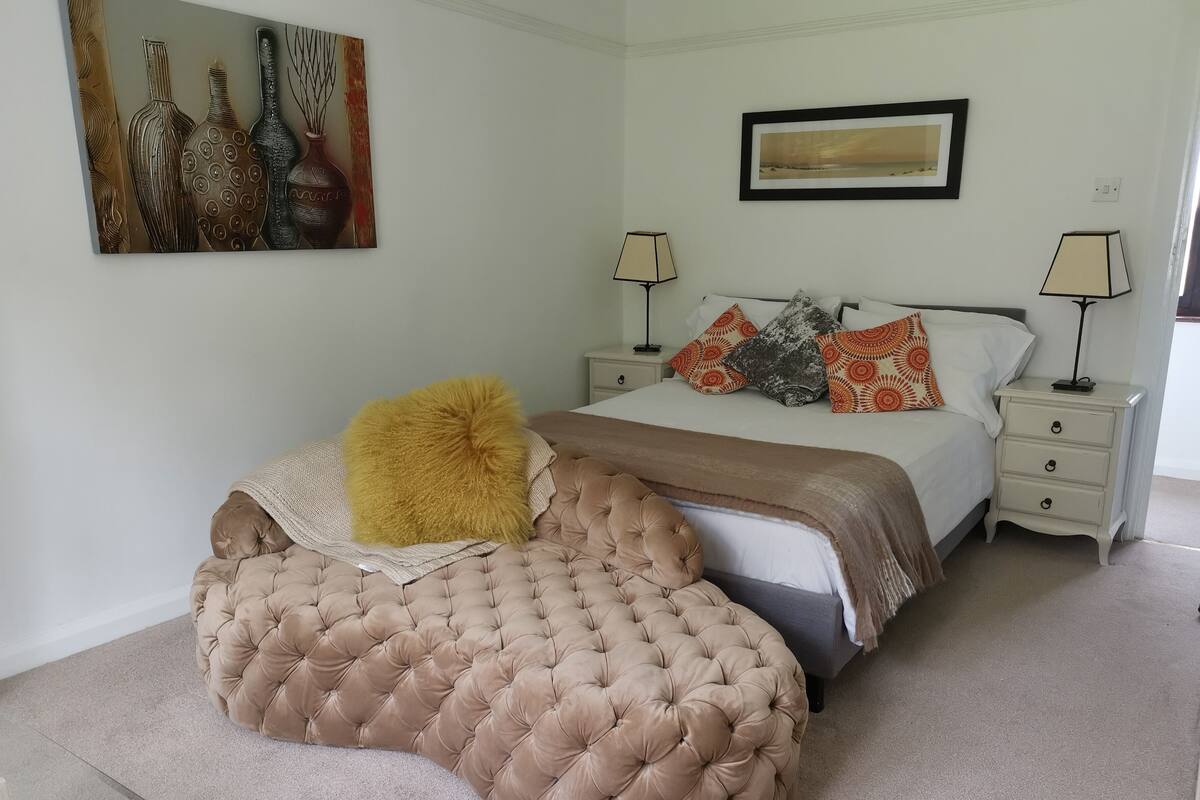 A bedroom with a large bed, two bedside tables, a nightstand, a painting, and a lamp.