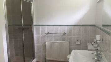 Un baño con cabina de ducha de vidrio, un lavamanos blanco con espejo y un inodoro.