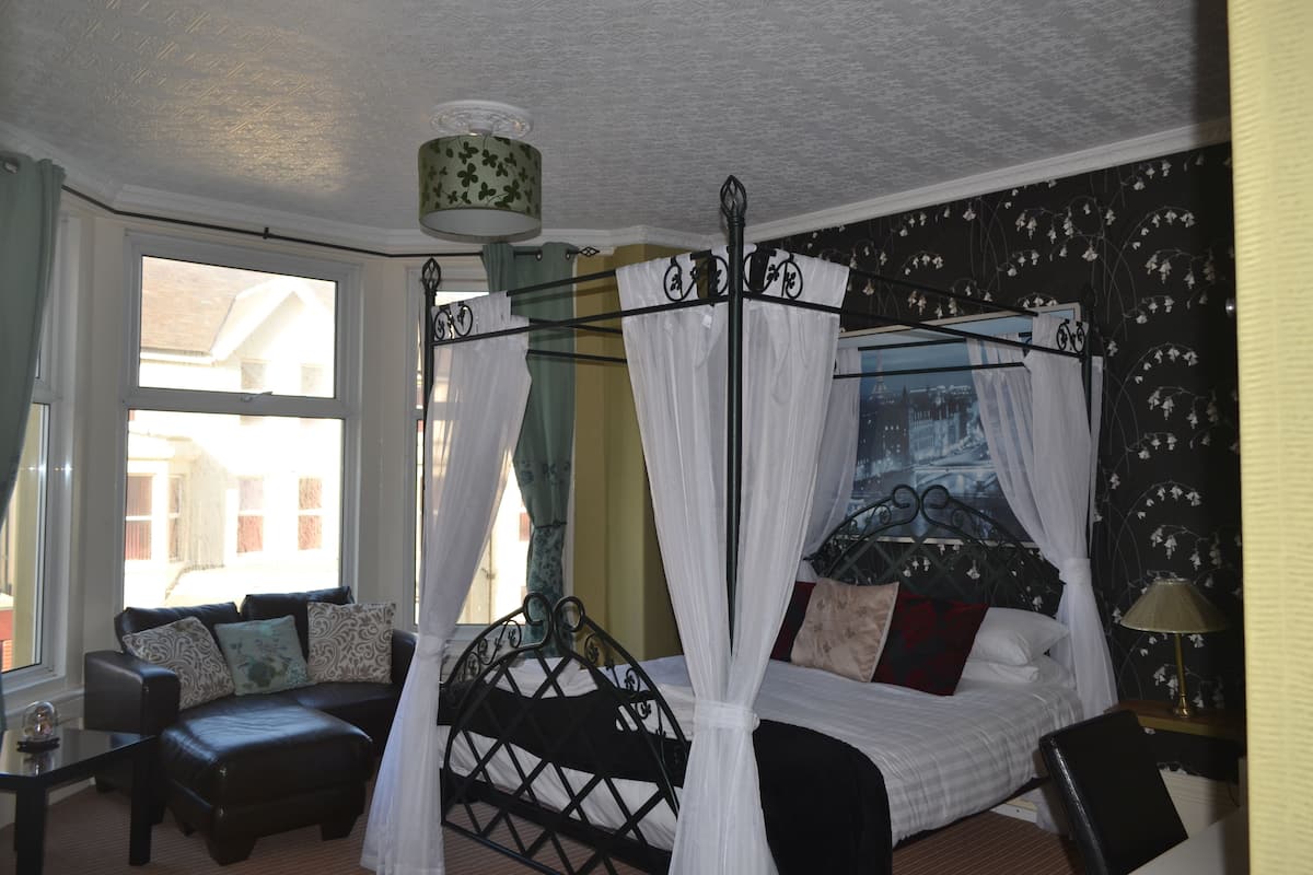 A bedroom with a four-poster bed, a sofa, and a window with curtains.
