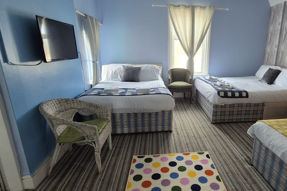 A hotel room with two beds, a television, a chair, a small table, and a polka dot rug.