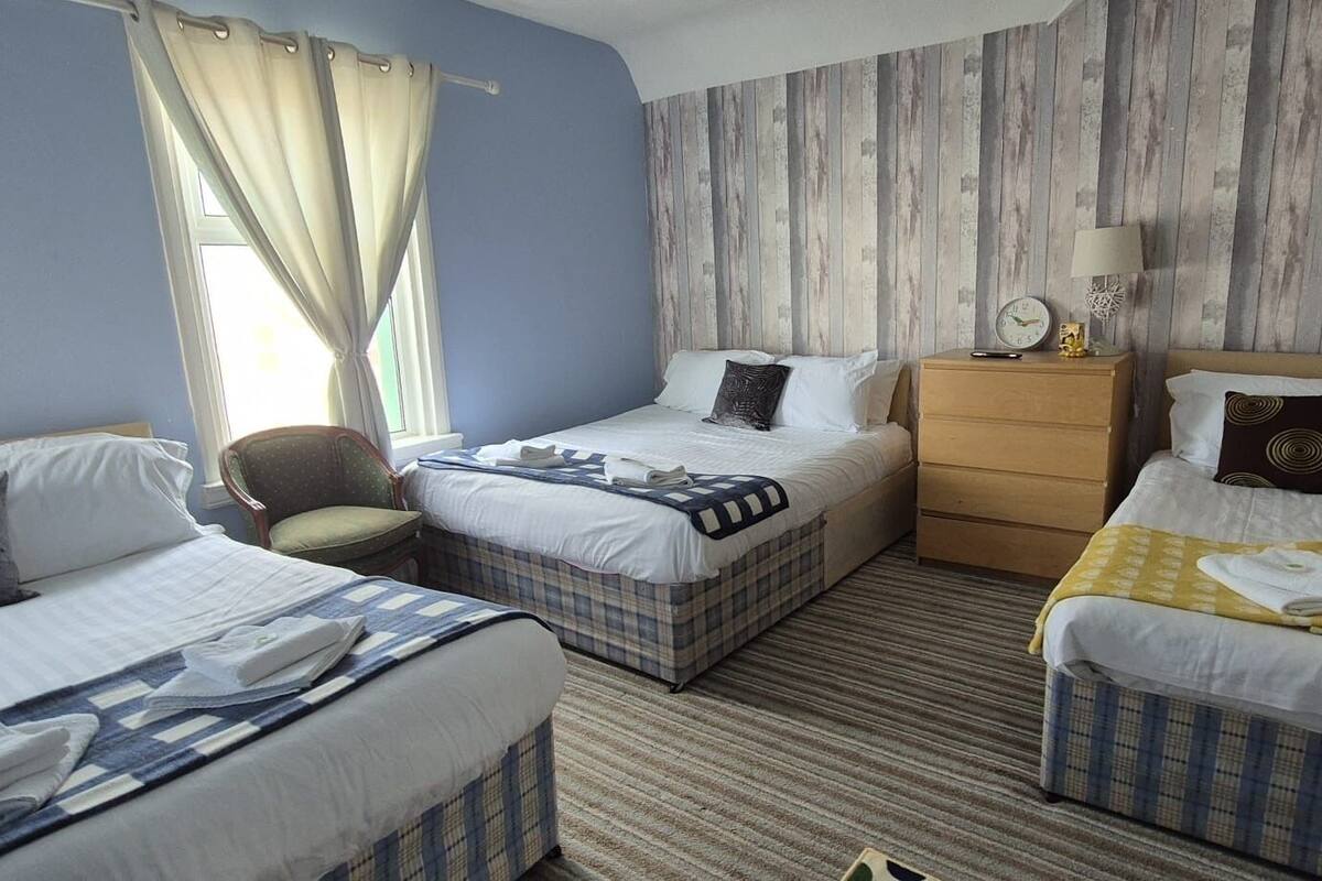 A hotel room with two single beds, a chair, a dresser, and a nightstand with a lamp.