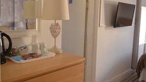 A room with a wooden dresser, a lamp, a tray with food items, a mirror, and a television mounted on the wall. - Holmlea Guest House (Blackpool)