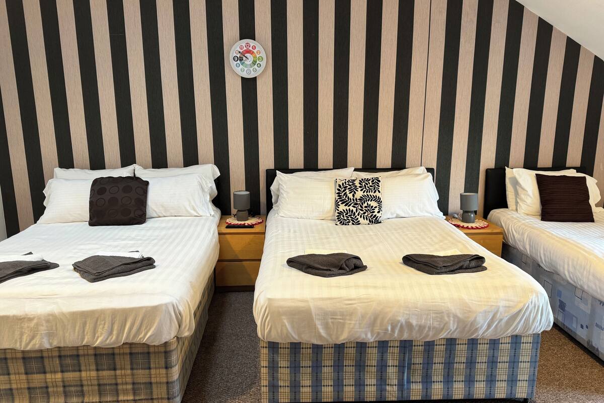 A hotel room with two single beds, a nightstand with a lamp, and a wall clock.