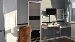 A compact hotel room with a checkered floor, a small desk with a kettle, a flat-screen TV, and a window with curtains. - Holmlea Guest House (Blackpool)