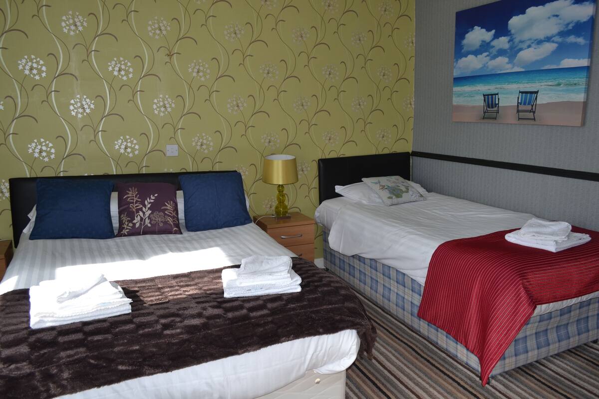 A hotel room with two beds, a nightstand, a lamp, and a painting of a beach scene.