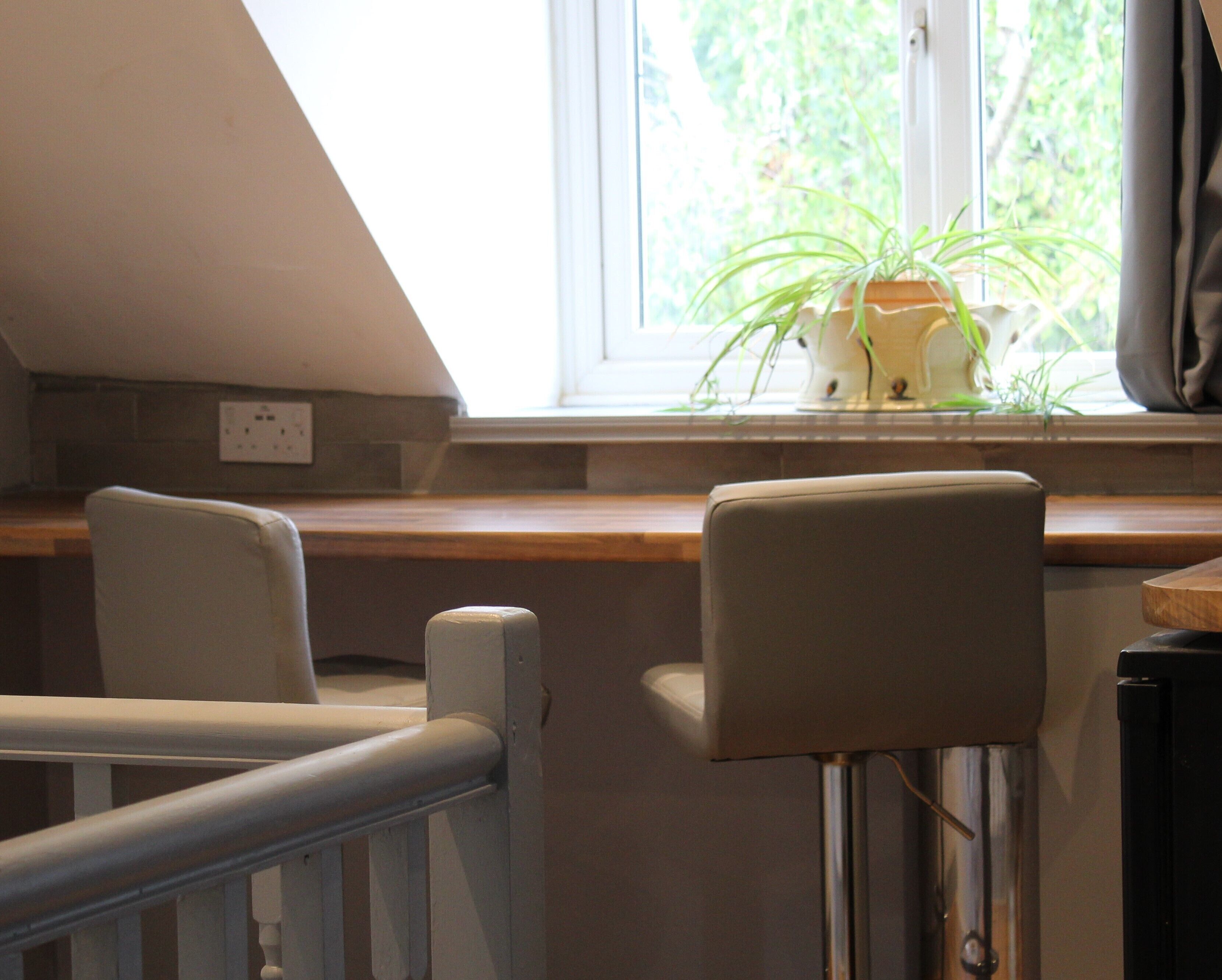 Una habitación con techo inclinado, una ventana con una planta en el alféizar, una silla blanca y un radiador.