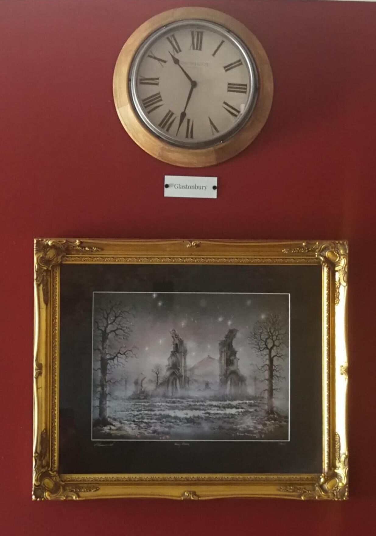 A clock with Roman numerals and a framed picture of a winter landscape.