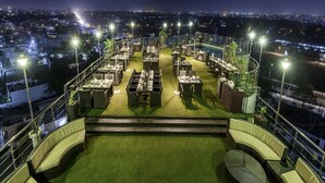 Un restaurante en la azotea con mesas al aire libre, piscina y vistas nocturnas de la ciudad.