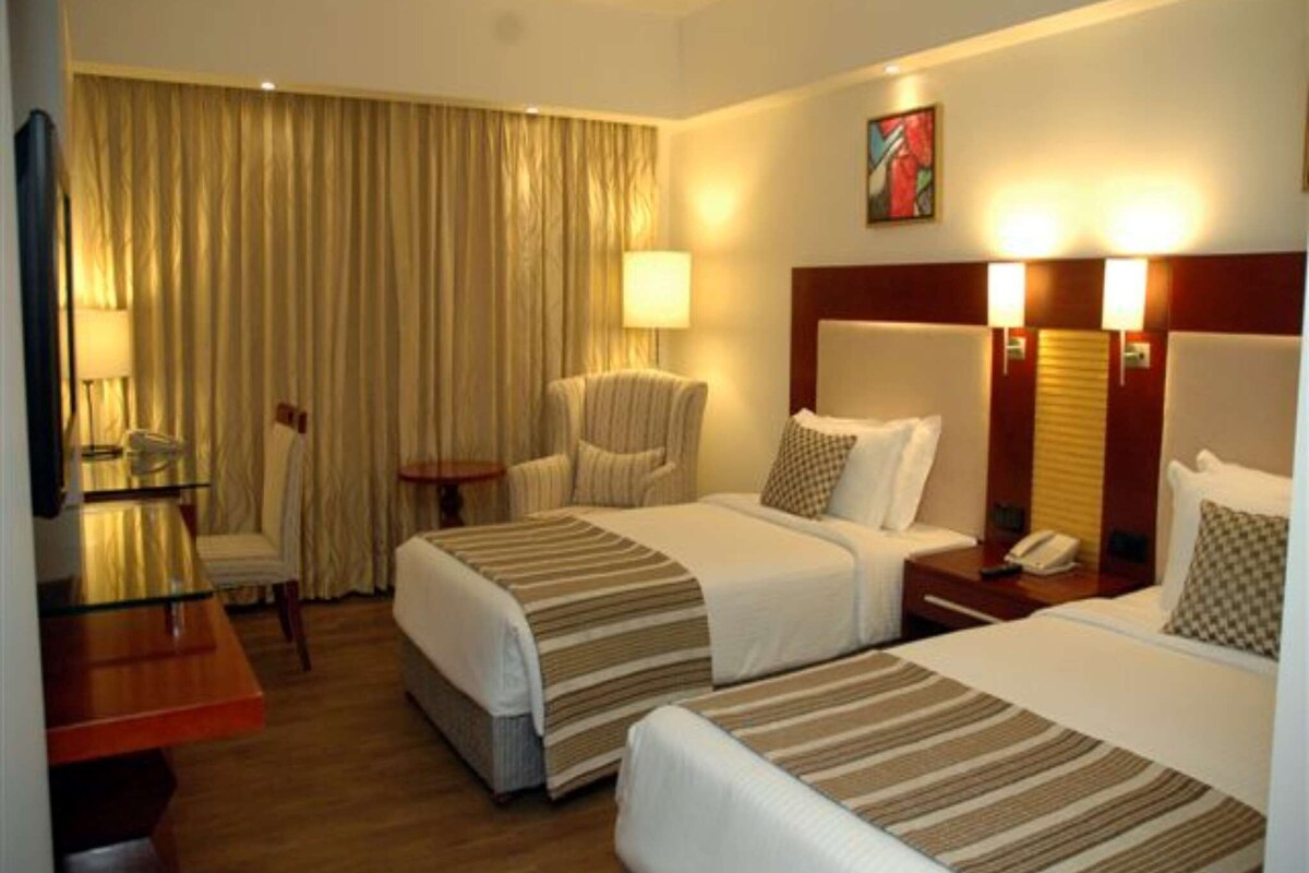 Habitación de hotel con dos camas, una silla, un escritorio y una lámpara.