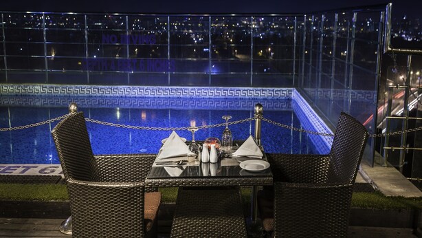 Un área de comedor al aire libre con sillas de mimbre y una mesa preparada para dos, con vistas a una piscina con un borde de mosaico azul.