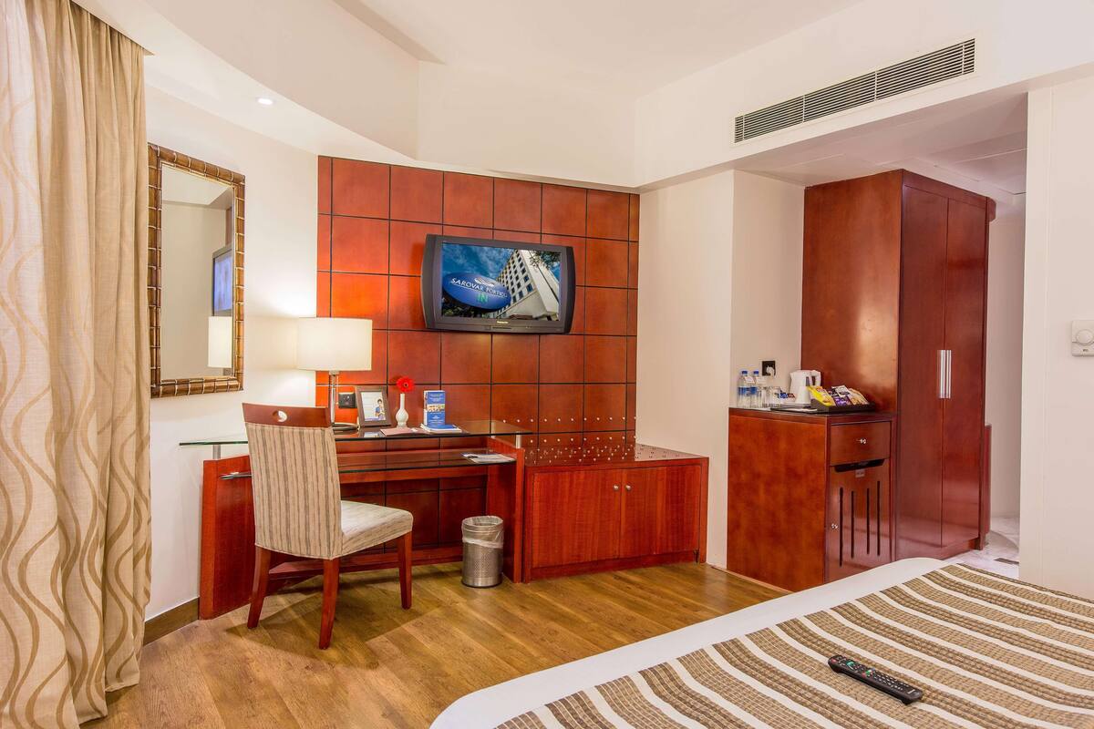 Une chambre d’hôtel comprenant un lit, un bureau avec une chaise, un téléviseur fixé au mur et une armoire.