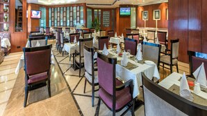 Un restaurante con varias mesas y sillas, una pantalla de televisión y una pared decorativa con un diseño estampado.