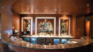 Una zona de bar con una barra de mármol curva, varios estantes con botellas y un escaparate central en arco.