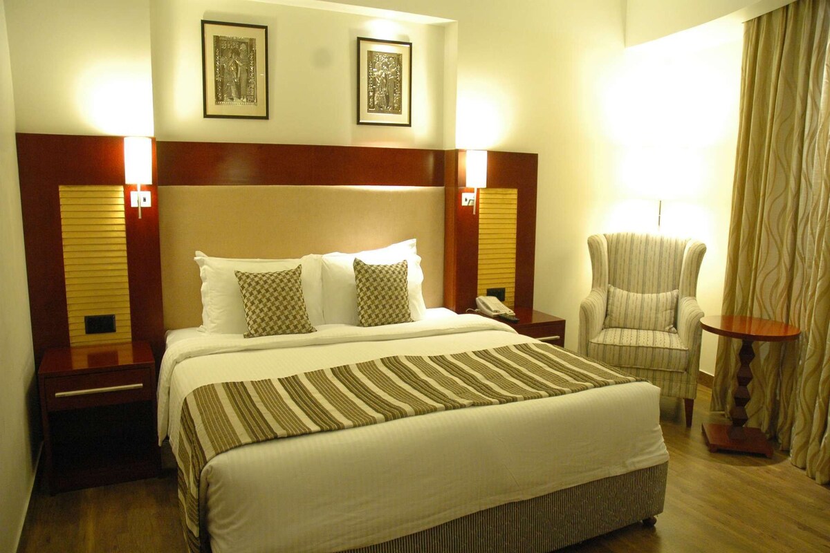 Una habitación de hotel con una cama grande, dos lámparas de noche, una silla y una mesita.
