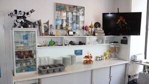 Balcão de café da manhã com geladeira, prateleiras com diversos itens, televisão e placa indicando buffet.