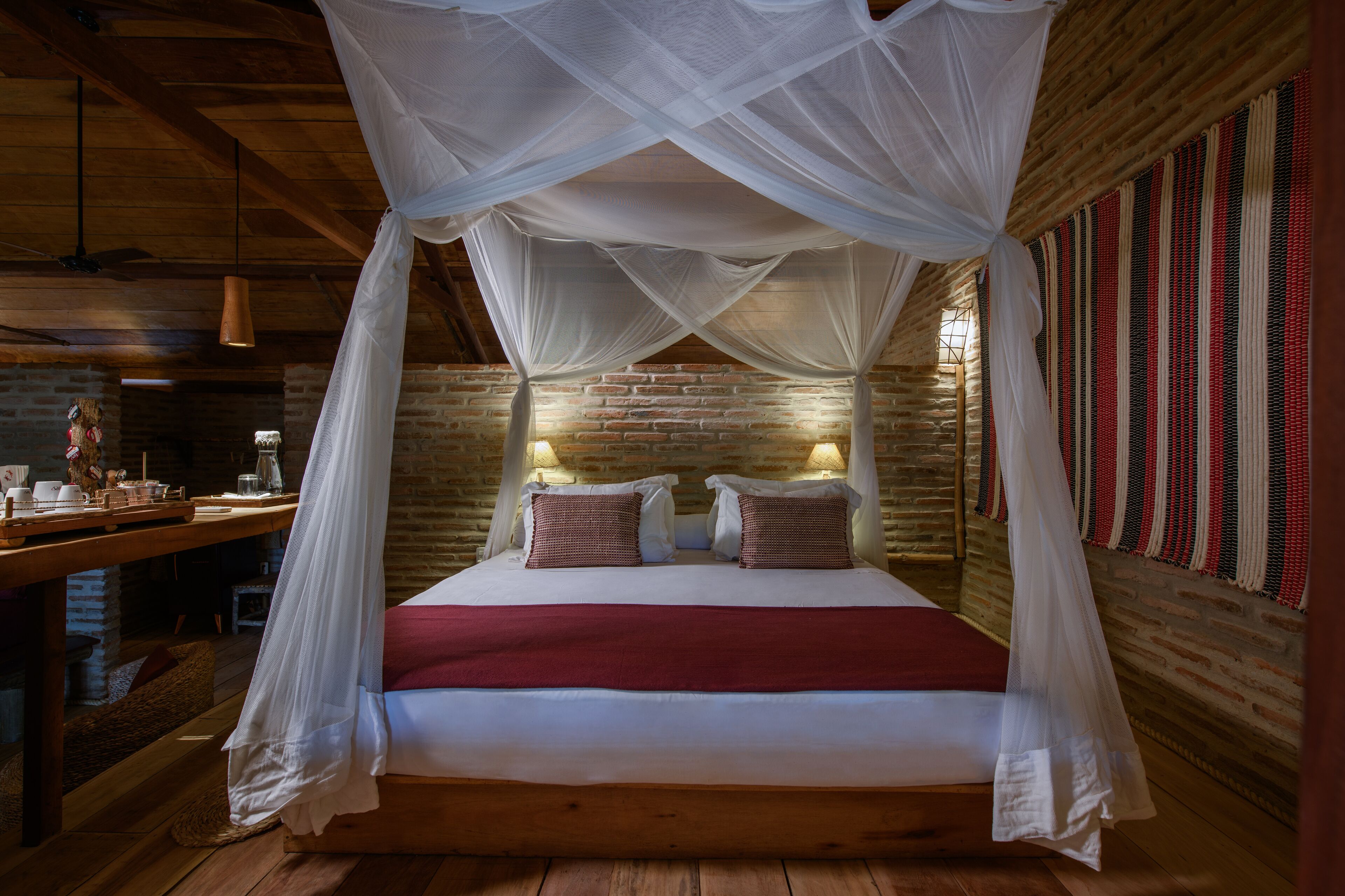A bed with a canopy, a brick wall, and a woven tapestry.
