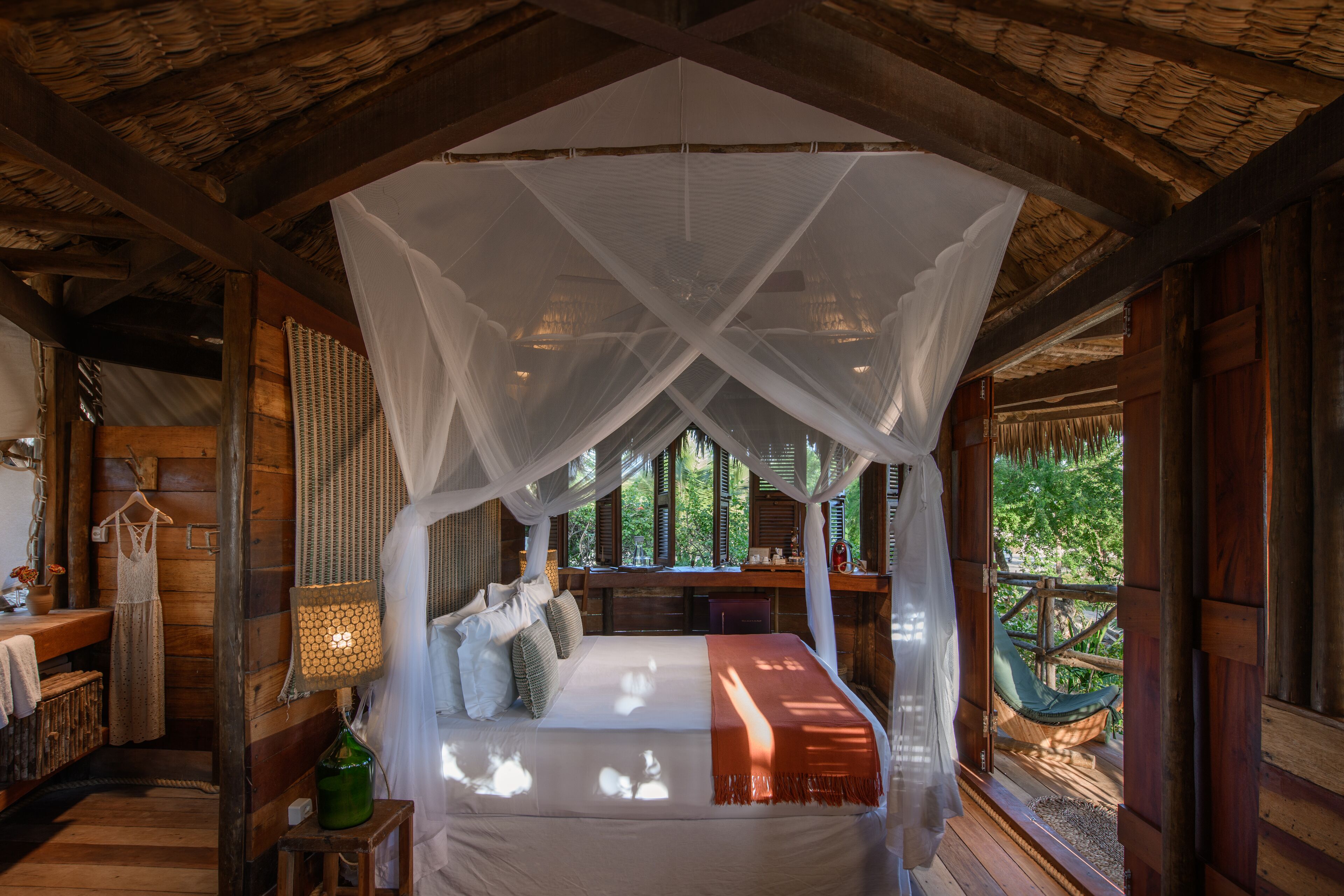 A bedroom with a canopy bed, wooden walls, a desk, and a view of greenery outside.