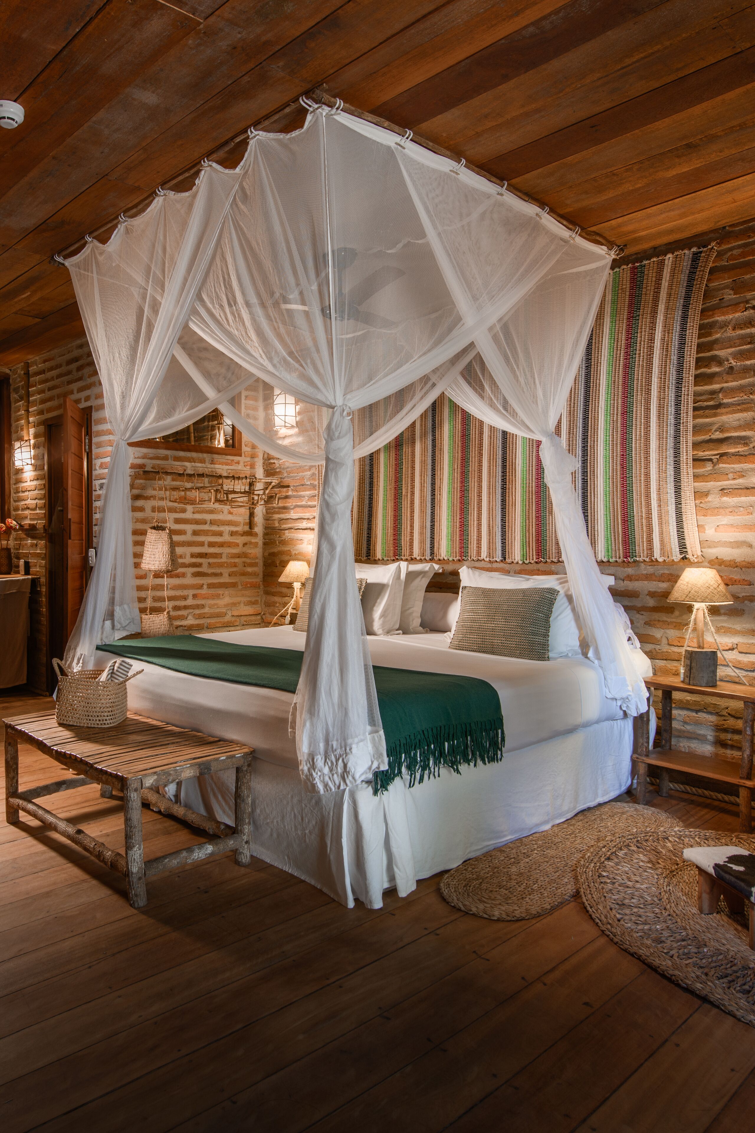 A room with a four-poster bed, wooden flooring, and a brick wall.