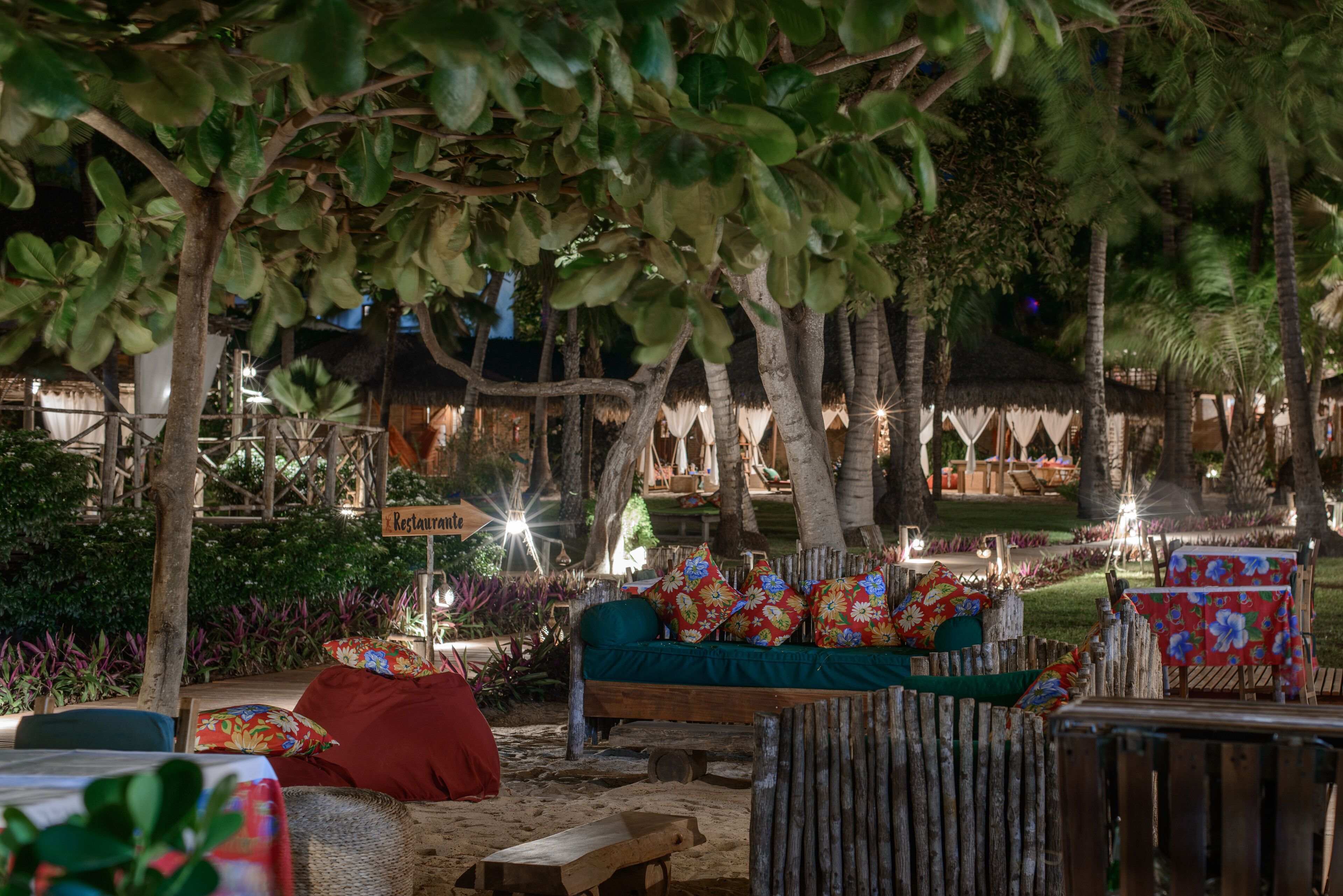 Un área de estar al aire libre con un banco de madera, una mesa con mantel floreado y un letrero que indica un restaurante.