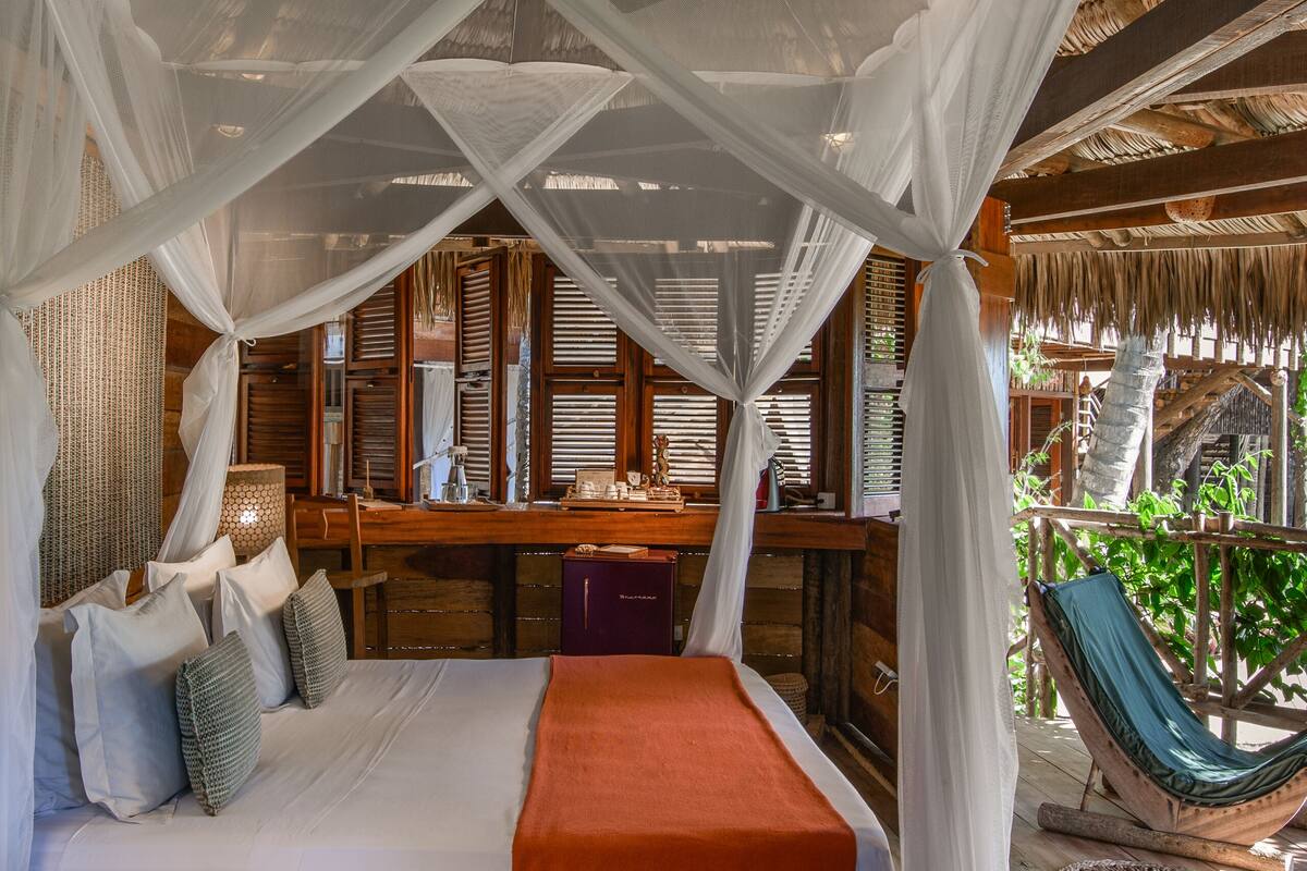 A room with a bed under a canopy, wooden furniture, and a view of the outdoors.