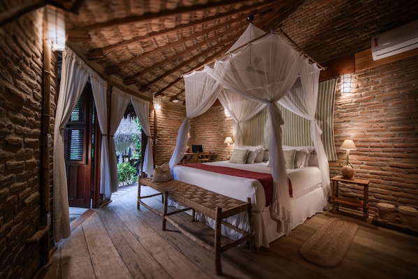 A rustic bedroom with a four-poster bed, wooden flooring, and a brick wall.