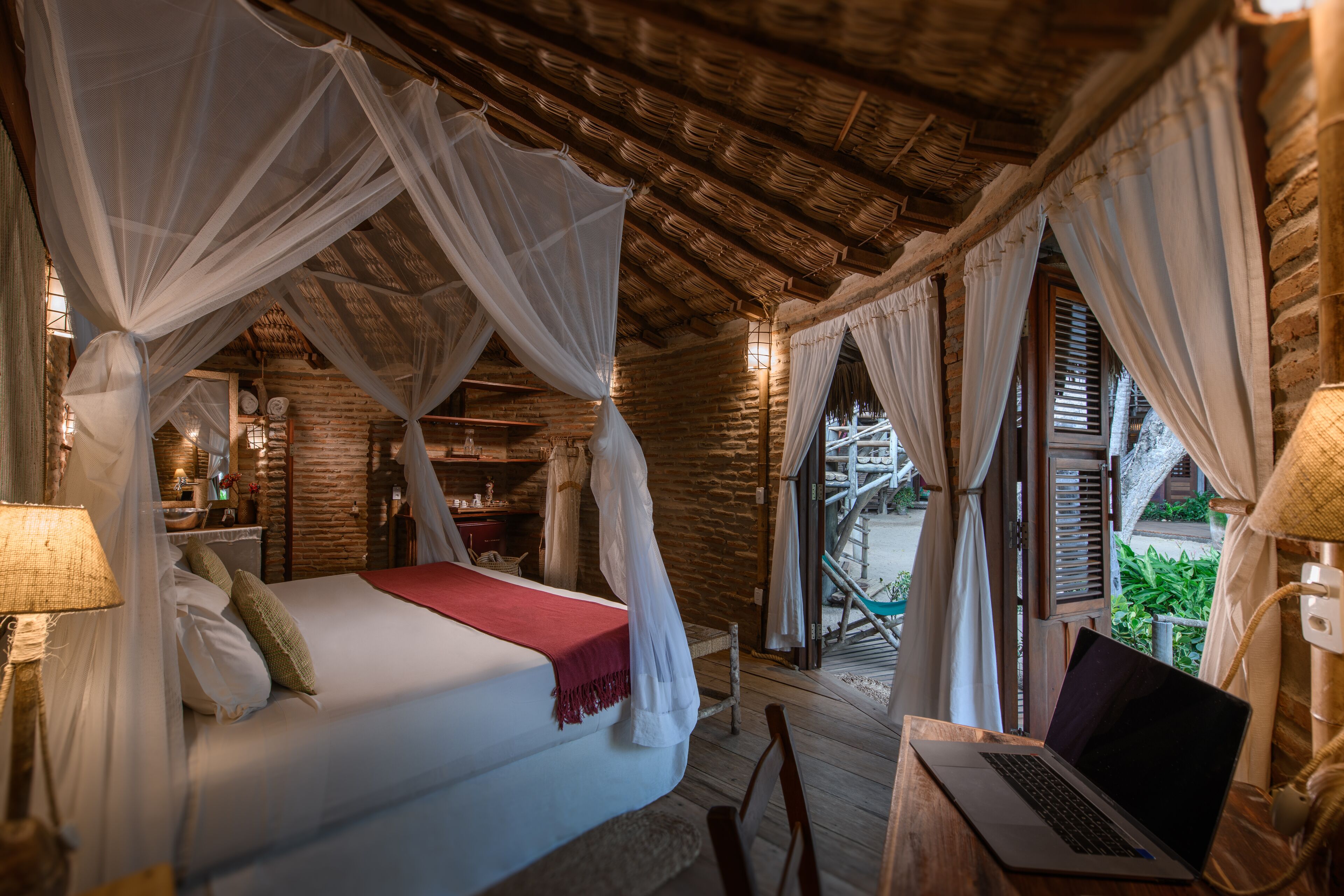 A room with a bed, a laptop on a table, and a view of the outdoors.