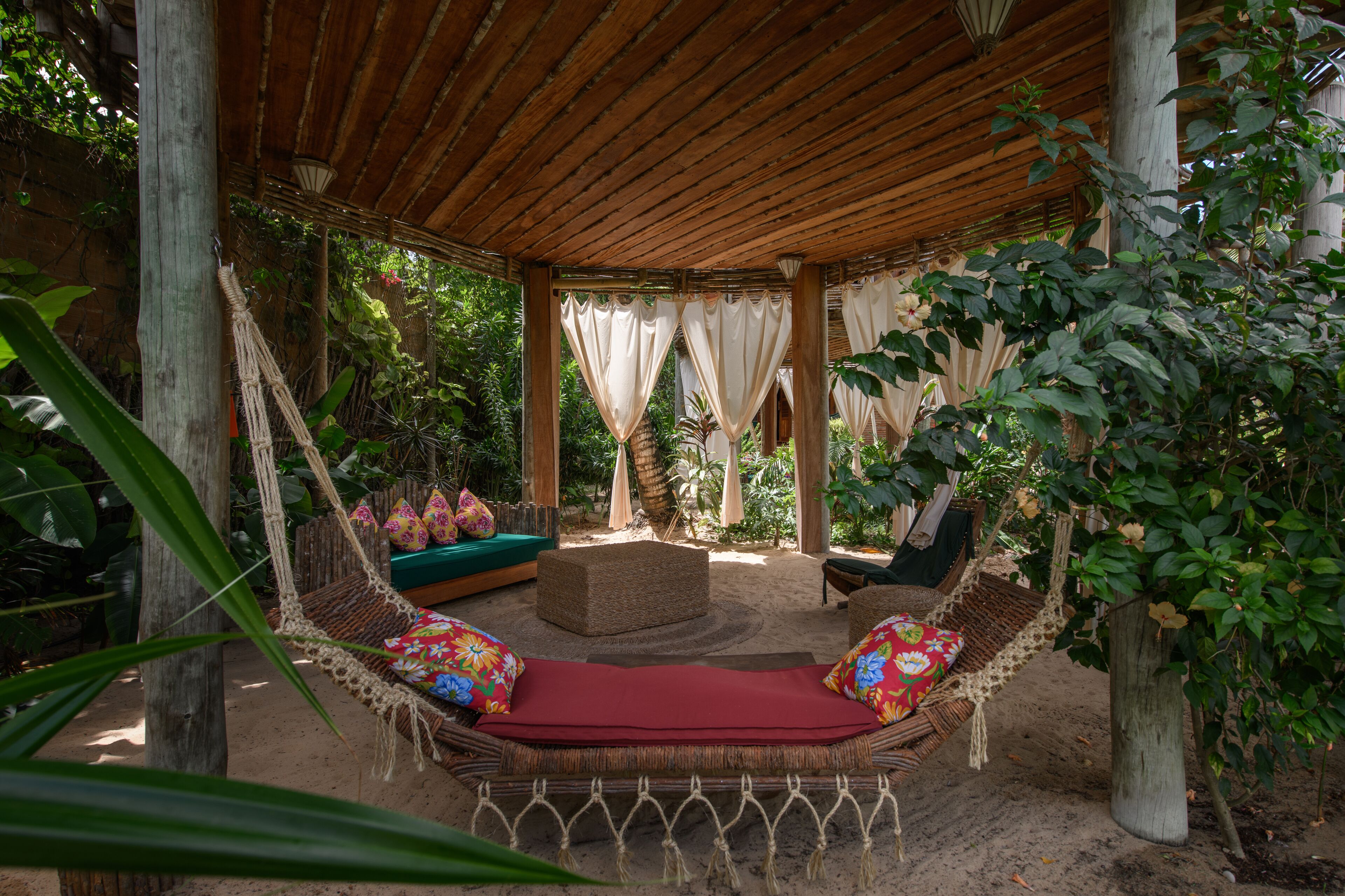 A covered outdoor seating area with a hammock, cushioned seating, and a wooden pergola structure.