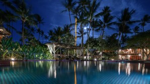 Un espace piscine aménagé pour la nuit, avec des palmiers et un coin salon abrité.