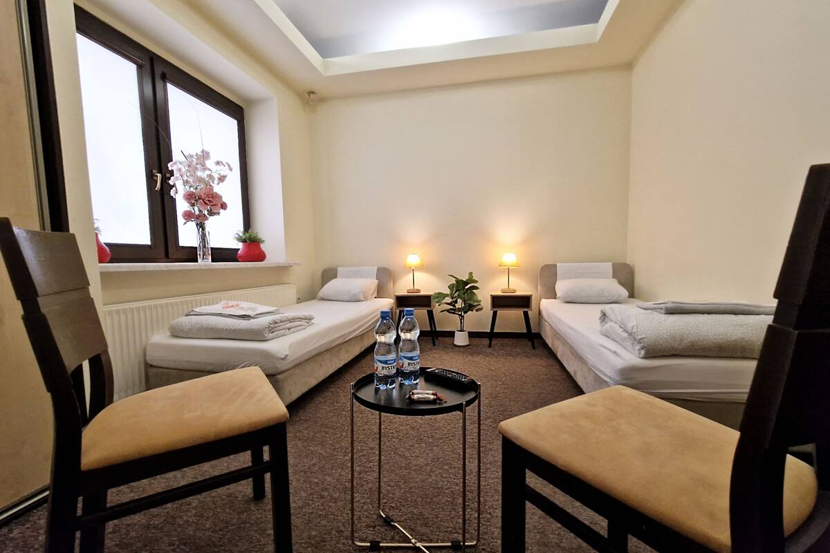 A hotel room with two single beds, a small table with a remote control, and a chair.