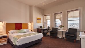 A hotel room with a bed, desk, two chairs, a small table, and a window with blinds. - Auldington Hotel (Launceston)