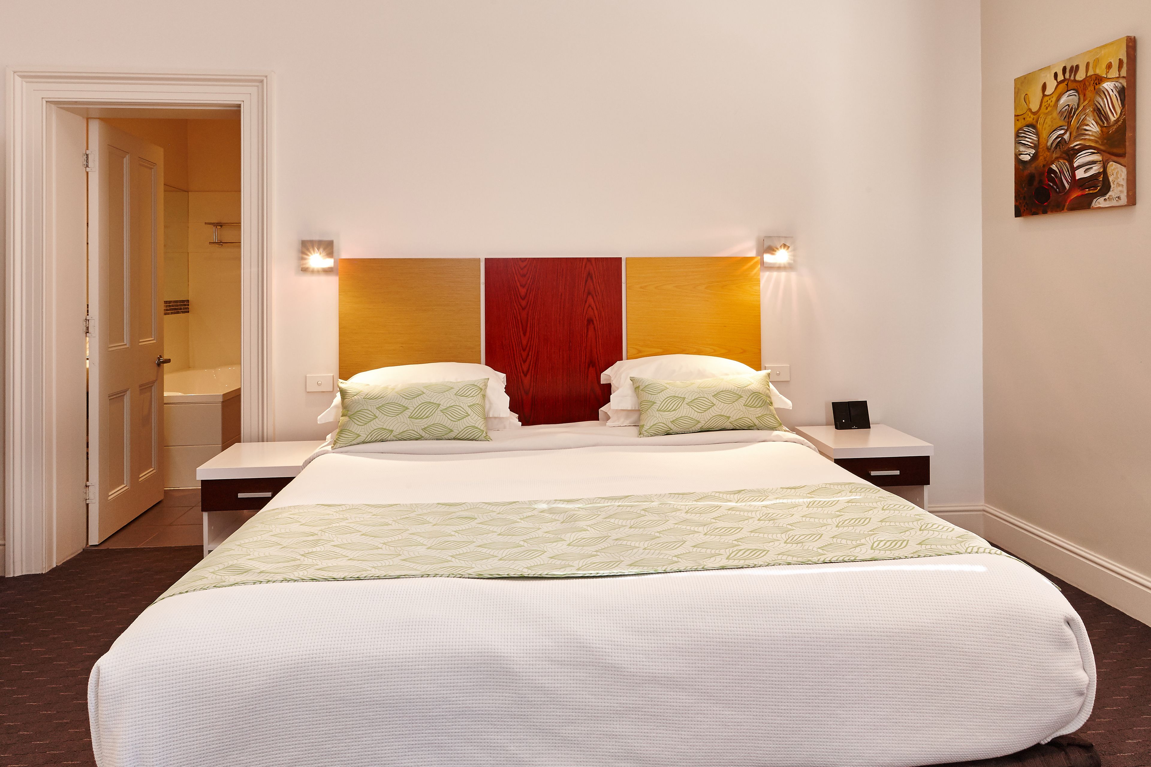 A hotel room with a large bed, two bedside tables, a nightstand, and a painting on the wall.