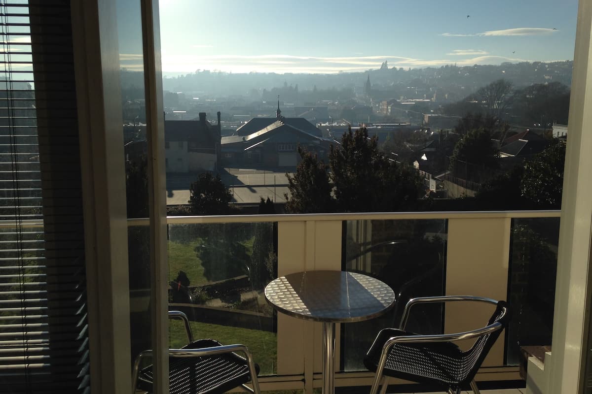 Un balcón con una mesa y dos sillas, con vista a una zona residencial con casas y una iglesia.