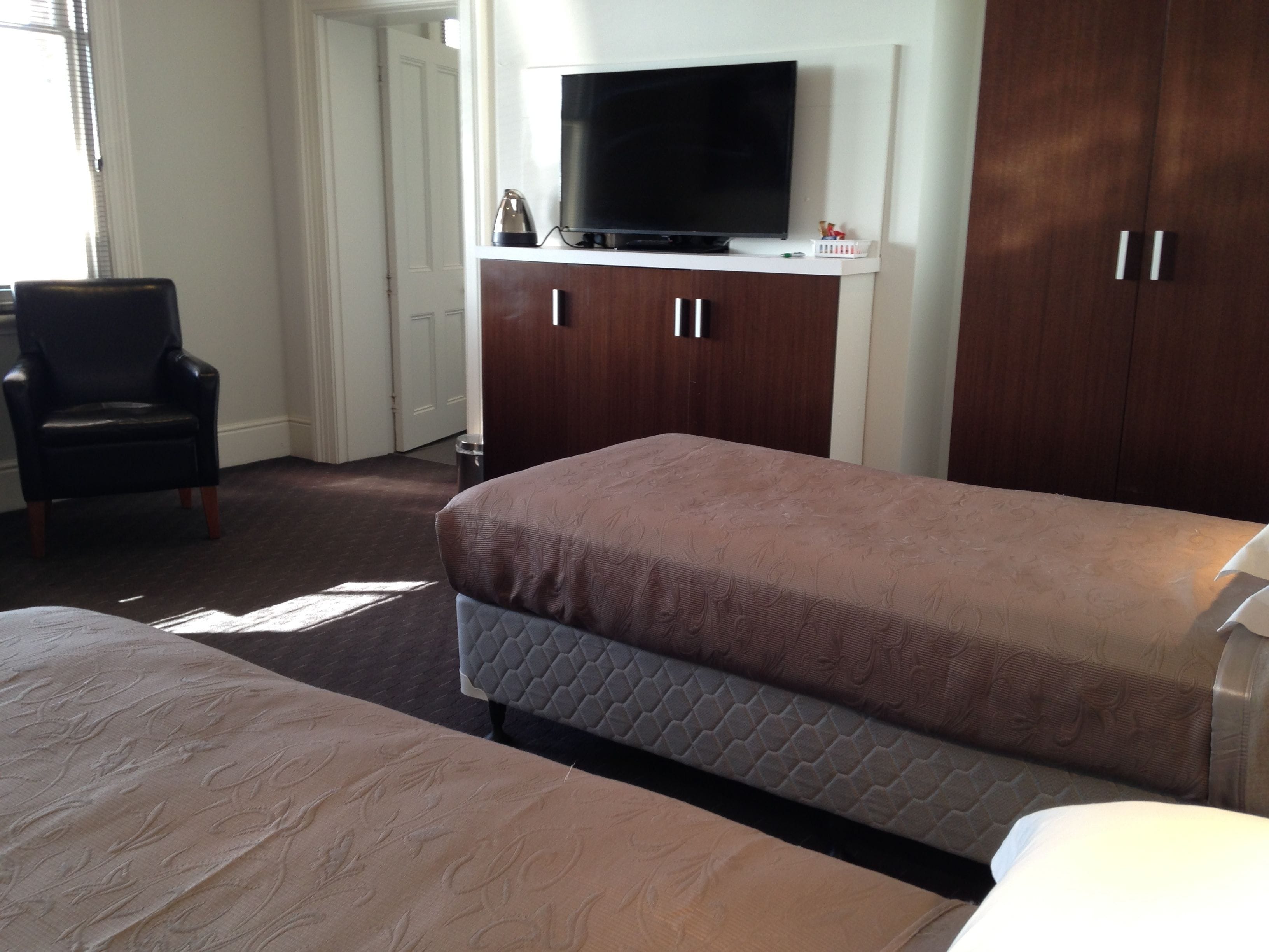 A hotel room with two beds, a TV on a wooden cabinet, a chair, and a door.