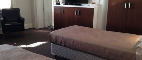 A hotel room with two beds, a TV on a wooden cabinet, a chair, and a door.