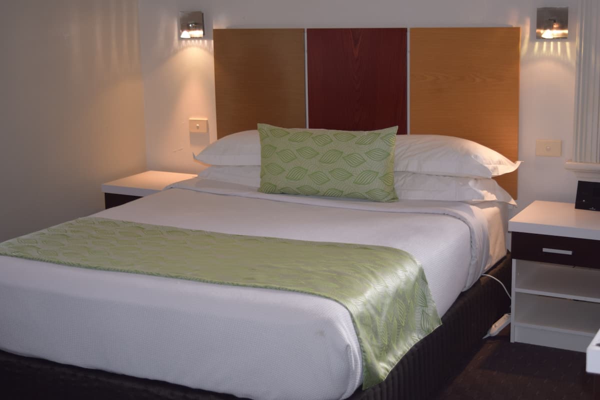 Habitación de hotel con una cama grande, cabecera de madera y dos mesitas de noche con lámparas.