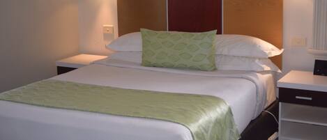 Habitación de hotel con una cama grande, cabecera de madera y dos mesitas de noche con lámparas.