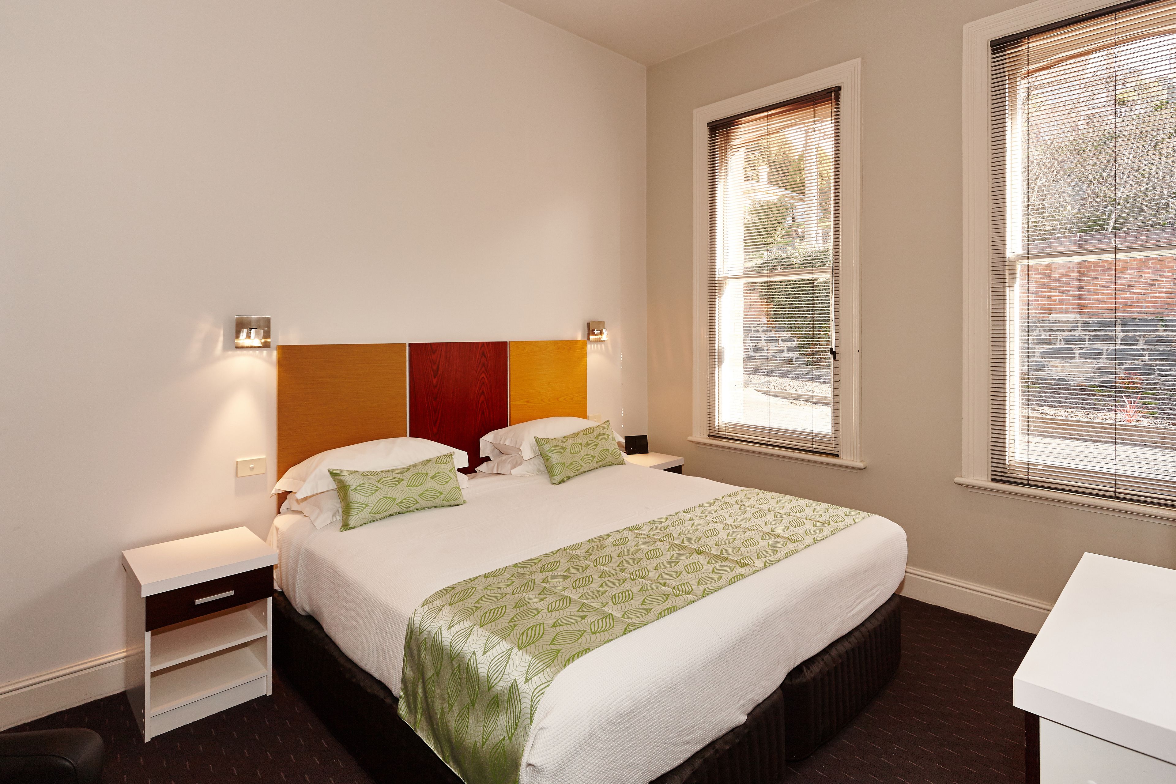 Una habitación de hotel con una cama, mesitas de noche y dos ventanas con persianas.