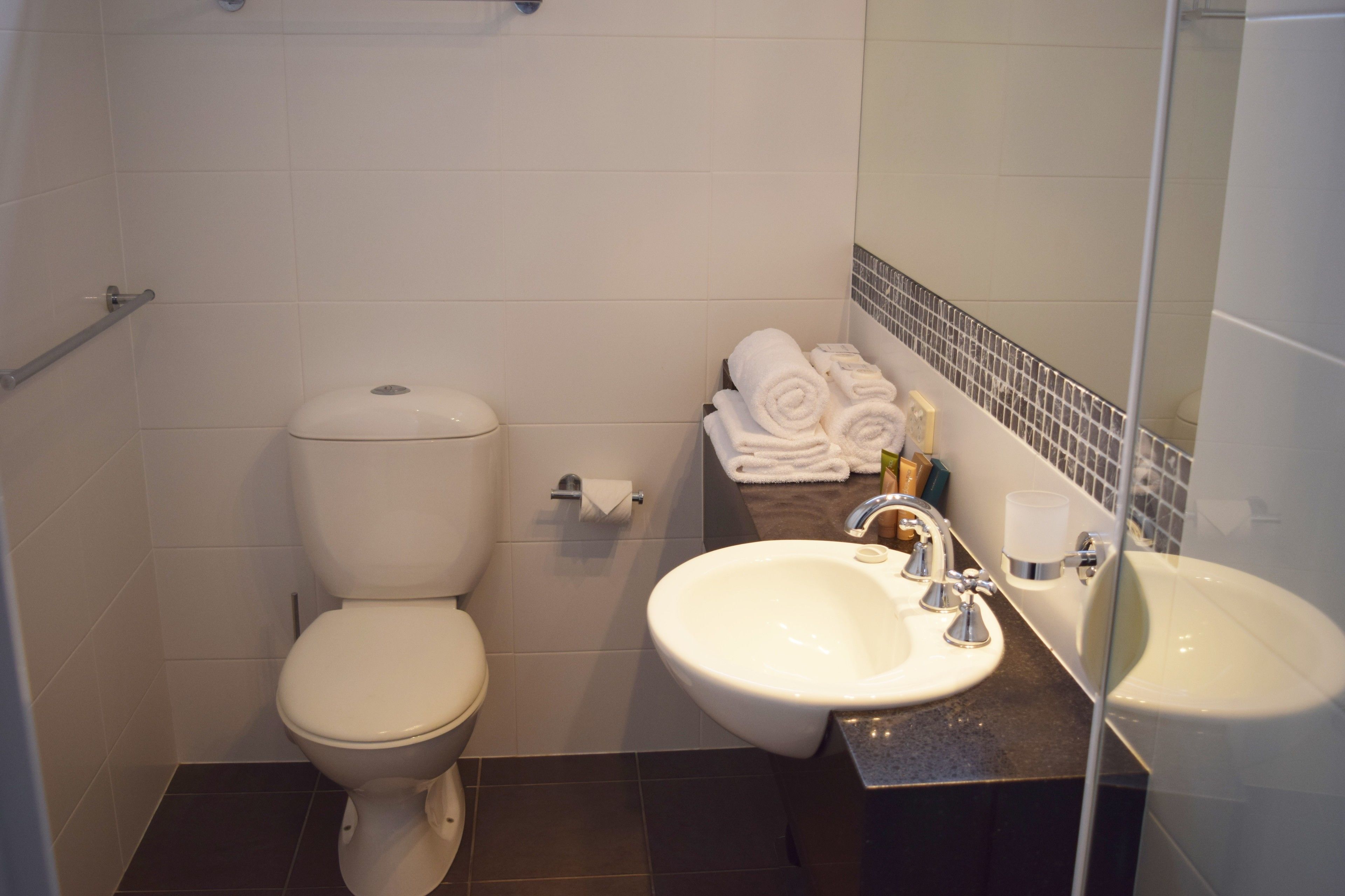 A bathroom with a toilet, sink, and a towel rack with towels.