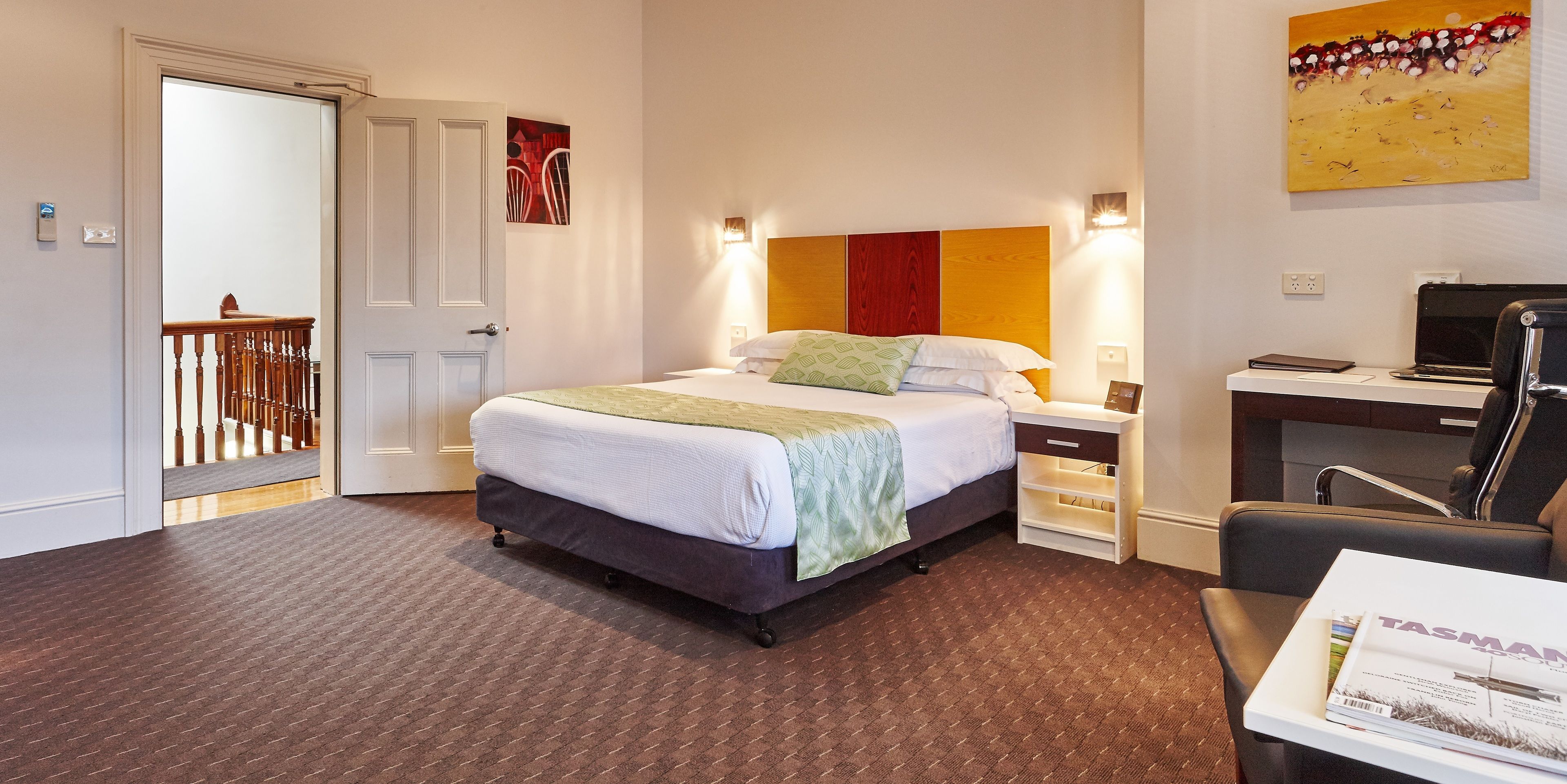 Een hotelkamer met een bed, een bureau met een stoel, een laptop en een tijdschrift op tafel.
