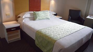 A neatly made bed with a patterned bedspread and pillows, a wooden headboard, bedside tables, and a chair.