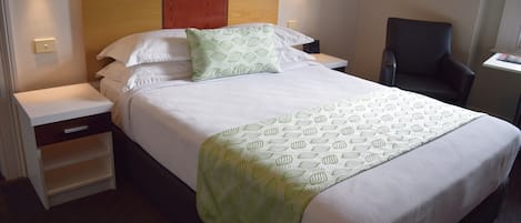 Una cama bien hecha con colcha y almohadas estampadas, un cabecero de madera, mesitas de noche y una silla.