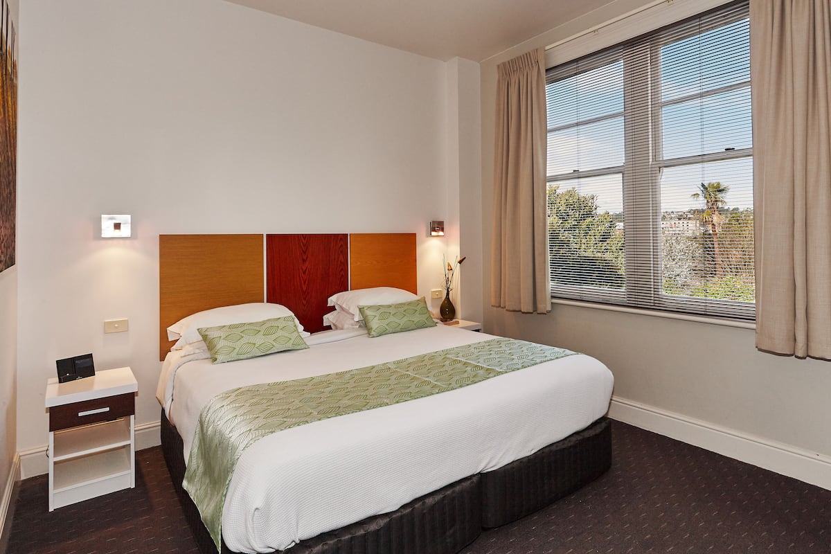 Una habitación de hotel ordenada con una cama grande, mesitas de noche y un ventanal con cortinas.