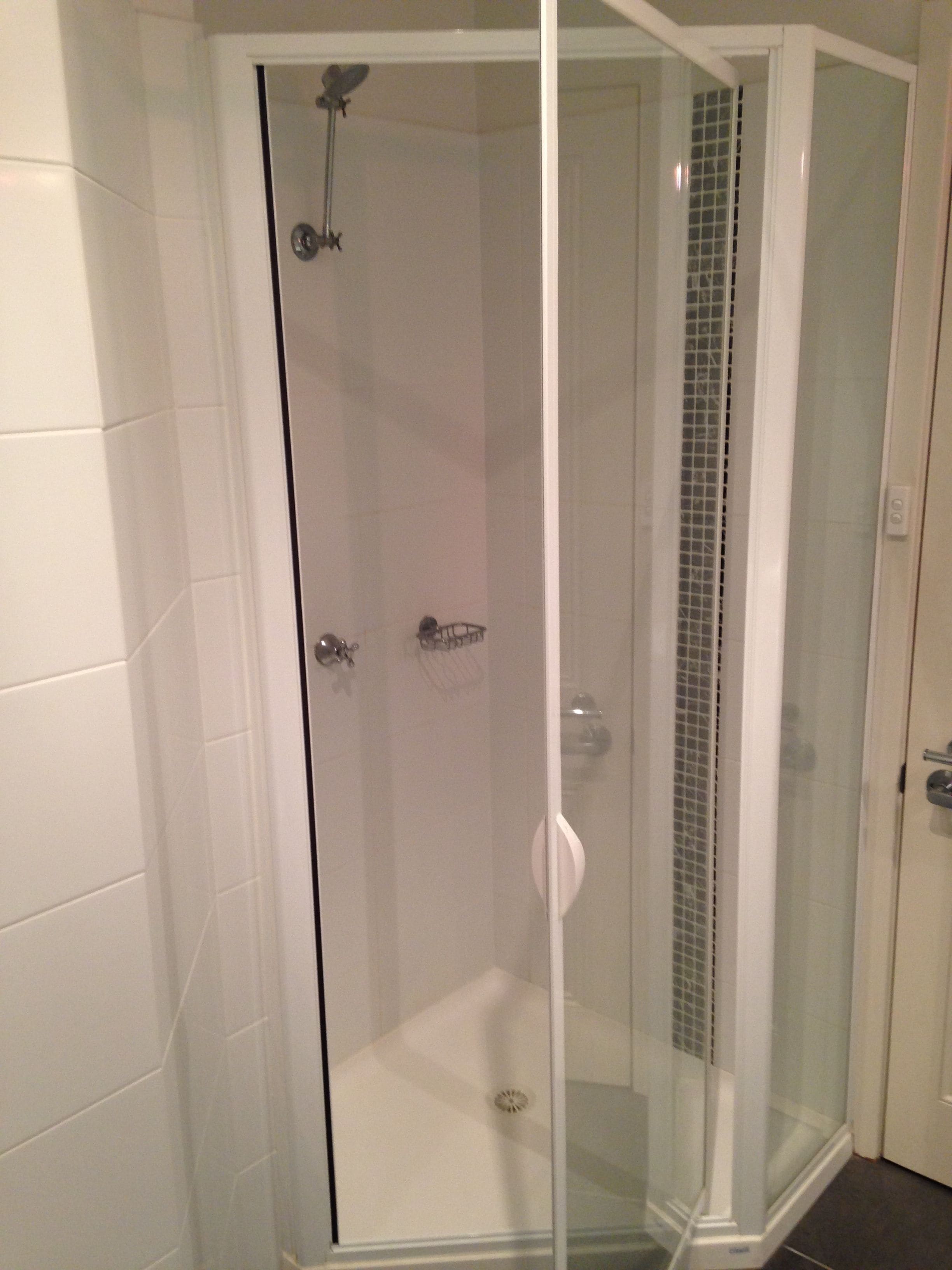 Una ducha con cerramiento de vidrio, pared de azulejos, cabezal de ducha y panel de control.