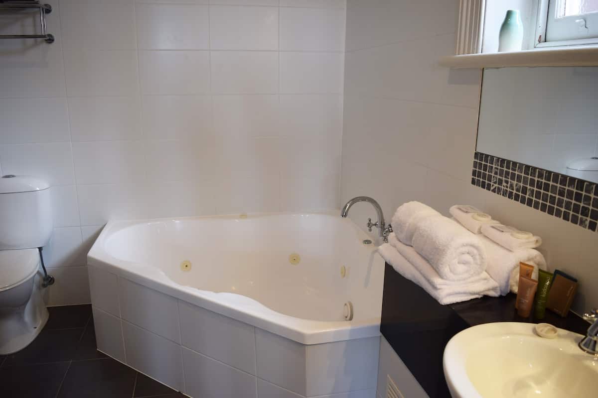 Un baño con bañera, inodoro, lavabo y un espejo con artículos de aseo.