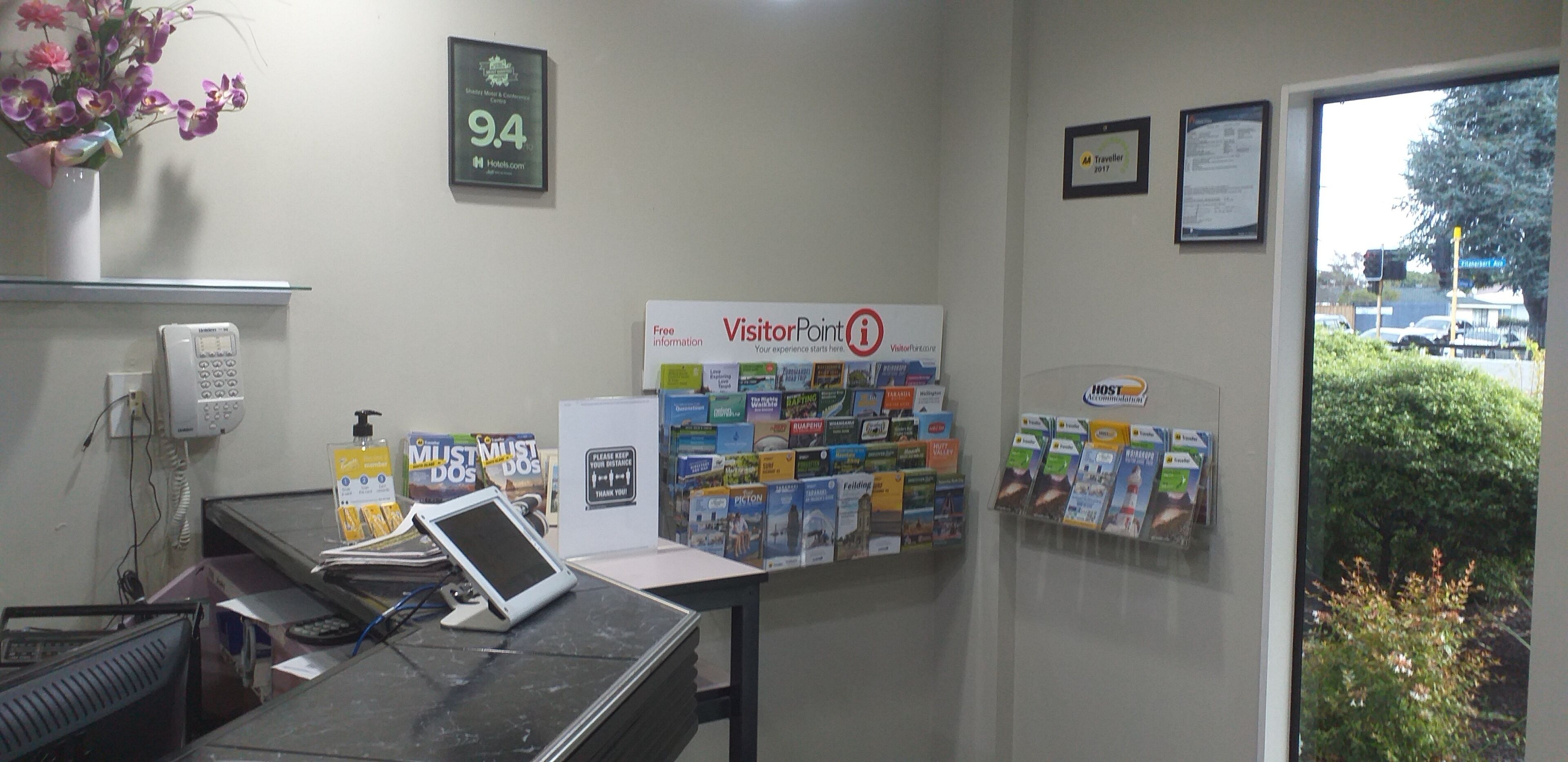 Un mostrador de recepción con una computadora, un teléfono y una pared que muestra varios folletos de viajes.