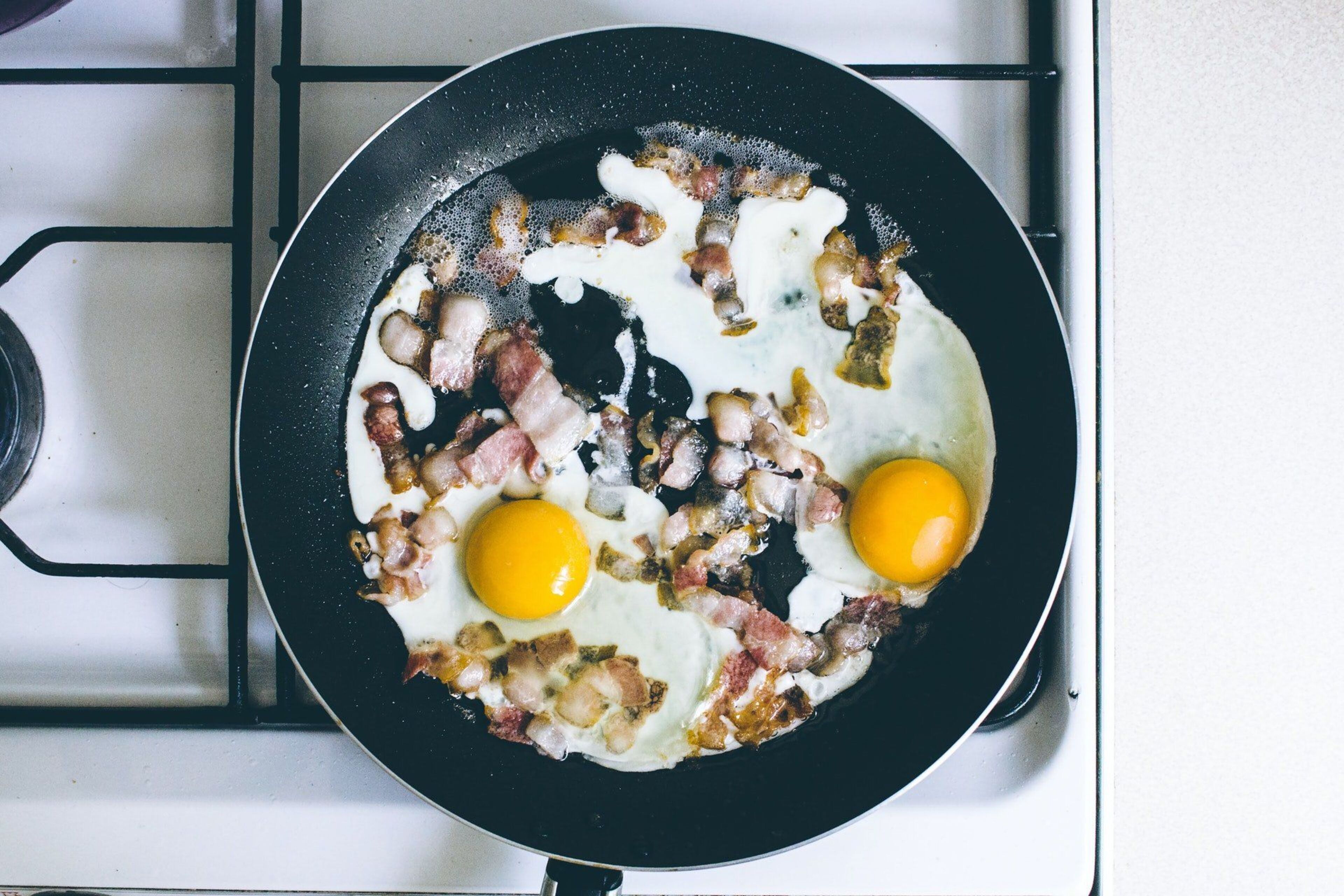 A frying pan with two eggs and bacon on a stove.