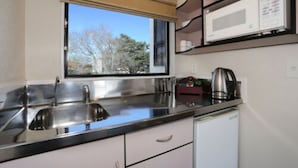 Cocina compacta con un lavamanos de acero inoxidable, un microondas y una tetera sobre la encimera.