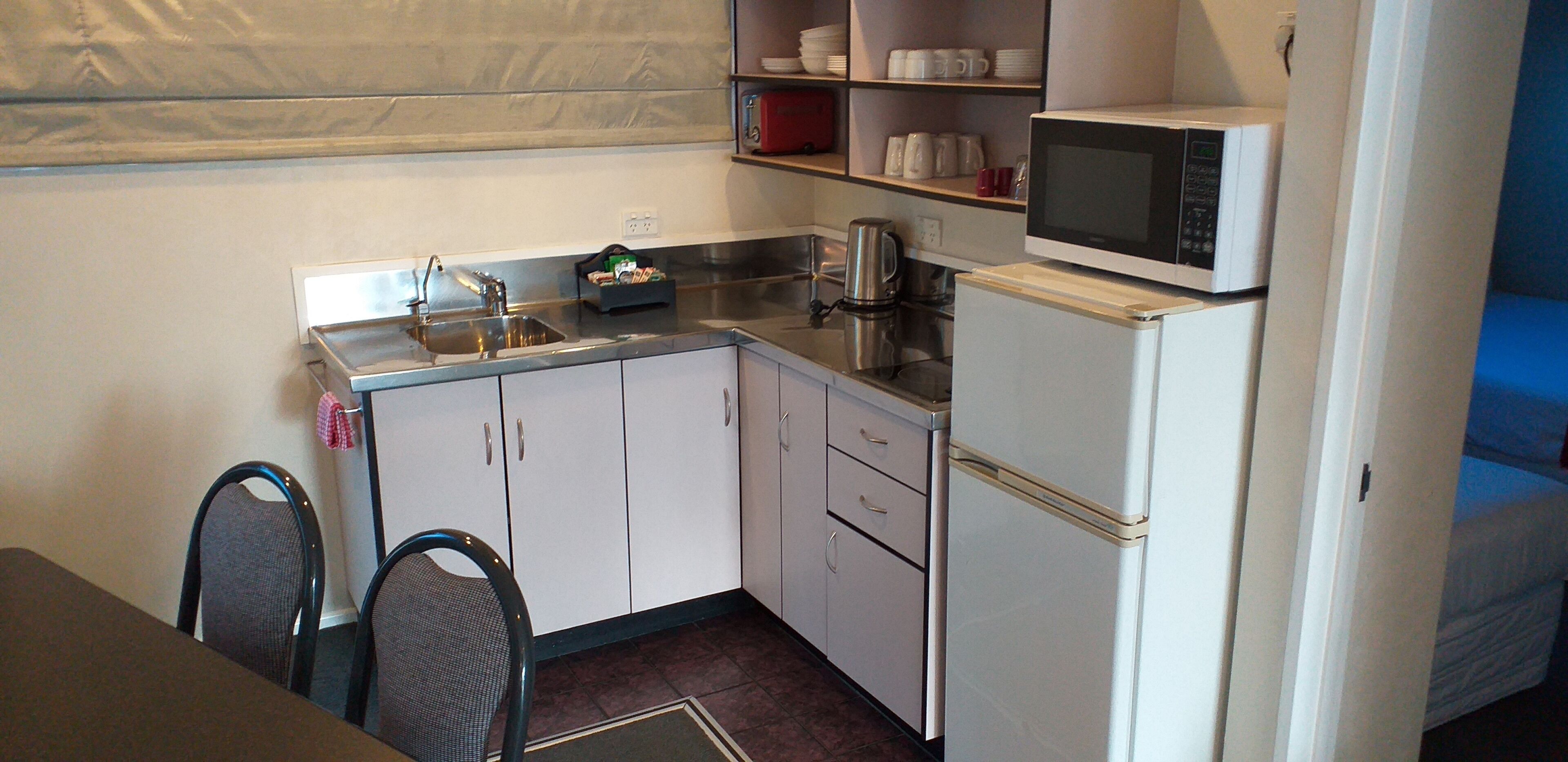 Cocina compacta con lavamanos, hervidor, microondas y refrigerador. Hay sillas y una mesa en la zona de comedor.