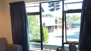 Una habitación de hotel moderna con un sofá gris, una mesita redonda pequeña, un escritorio blanco y ventanas grandes con cortinas.