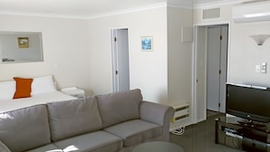 Una habitación de hotel moderna con una cama, un sofá gris, un televisor y una mesita.